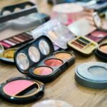 A variety of colorful makeup palettes and cosmetics organized on a wooden table.