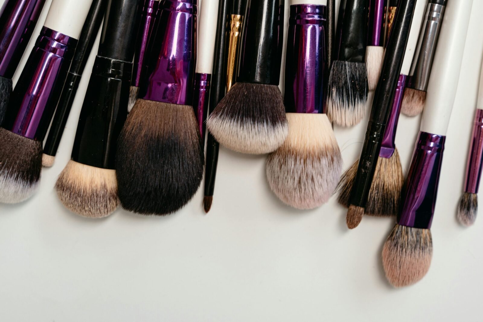 A collection of makeup brushes with soft bristles arranged on a white background in a flat lay style.